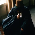 Personne Assise avec un Chapeau et un Bâton dans une Pièce Eclairée par la Lumière Naturelle