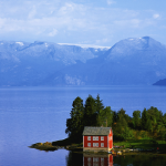Maison rouge au bord d'un lac avec montagnes en arrière-plan