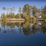 Maison isolée sur une île avec des arbres et un reflet dans l'eau