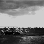 Plage animée avec voiture classique sous un ciel nuageux