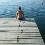 Femme en maillot assise sur un ponton en bois au bord de l'eau
