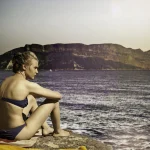 Femme en maillot de bain regardant la mer au coucher du soleil
