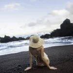 Femme en chapeau assise sur une plage volcanique
