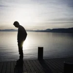 Silhouette d'un homme pensive au bord d'un lac au coucher du soleil