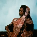 Femme enroulée dans un châle coloré contre un mur bleu