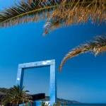 Cadre bleu géant sur plage ensoleillée avec plantes et palmiers