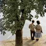 Couple se tenant par la main au bord de l'eau sous un arbre