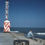 Pêcheur assis sur le quai à côté du phare rayé rouge et blanc