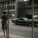 Femme en robe attend à un passage piéton, voiture verte passant