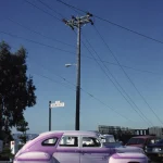 Voiture classique rose sur une rue avec poteau électrique