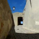 Ruelle en pierre menant à une porte voûtée sous un ciel bleu