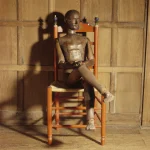Statue en bois assise sur une chaise dans une pièce en bois
