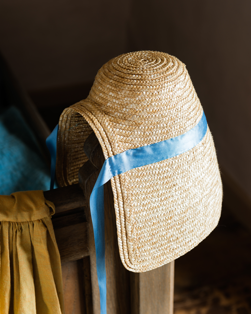 AKG4208361.webp Chapeau de paille avec ruban bleu accroché à une chaise – Image 1
