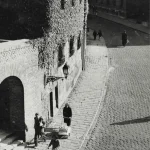 Scène de rue pavée en noir et blanc avec passants et poussettes