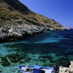 Petit bateau sur une eau turquoise près d'une falaise rocheuse