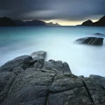 Paysage côtier calme avec rochers et montagnes sous un ciel couvert