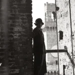 Femme en robe se tenant près d'un mur en brique avec une tour en arrière-plan