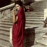 Femme en robe rouge photographiant sur un escalier en pierre