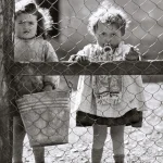 Enfants derrière un grillage avec un seau