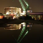Grue et bâtiment industriel illuminés la nuit avec réflexion sur l'eau