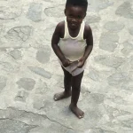 Enfant souriant debout sur un sol pavé