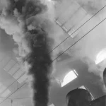 Locomotive à vapeur sous une verrière avec colonne de fumée
