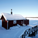 Petite cabane en bois rouge couverte de neige au bord d'un lac gelé
