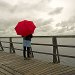 Personne avec parapluie rouge sur pont en bois au bord du lac