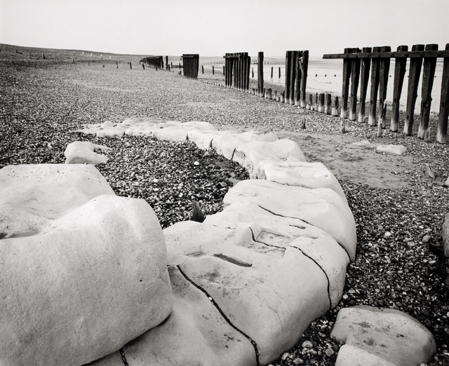 AKG5333675.webp Plage Rocailleuse avec Pilotes de Bois – Image 1