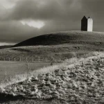 Maison solitaire sur une colline sous un ciel nuageux en noir et blanc