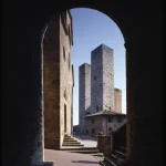 Vue à travers une arche sur une place avec des tours médiévales