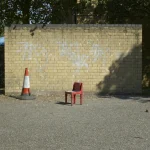 Chaise Rouge en Plastique et Plot de Signalisation devant un Mur en Brique