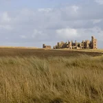 Ruines du château en plaine herbeuse sous un ciel nuageux