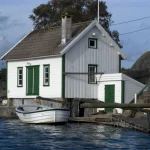 Maison en bois blanche et verte au bord de l'eau avec un bateau