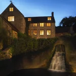 Maison en pierre avec chutes d'eau illuminée à la tombée de la nuit