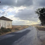 Maison abandonnée en bord de route sous un ciel nuageux
