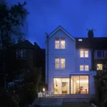 Maison éclairée la nuit avec une personne visible à l'intérieur.
