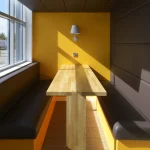 Coin repas lumineux avec banquettes noires et murs jaunes