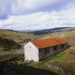 Vieille Bâtisse en Pierre à Toit Rouille dans les Collines Verdoyantes