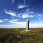Croix en pierre dans une lande sous un ciel bleu