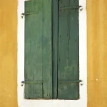 Fenêtre avec volets verts sur un mur jaune