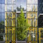 Édifice moderne avec piétons devant des vitrages réfléchissants et un arbre central