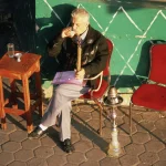 Homme buvant du thé et fumant une chicha en extérieur