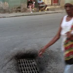 Rue urbaine avec égout et passants.