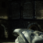 Tête sculptée en pierre devant un bâtiment en briques