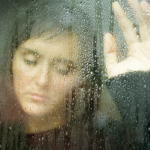 Jeune femme triste derrière une vitre mouillée