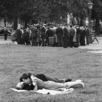 Couple allongé sur l'herbe devant un groupe de personnes dans un parc