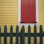 Fenêtre rouge avec clôture en bois vert sur maison jaune