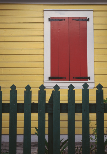 AKG5766762.webp Fenêtre rouge avec clôture en bois vert sur maison jaune – Image 1