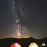 Ciel étoilé avec tentes éclairées dans un paysage nocturne